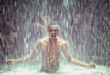 Homem tomando banho de cachoeira, feliz e imerso na natureza, com água caindo ao seu redor, representando a prática de Shinrin-yoku ou banho de floresta.