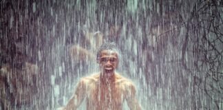 Homem tomando banho de cachoeira, feliz e imerso na natureza, com água caindo ao seu redor, representando a prática de Shinrin-yoku ou banho de floresta.