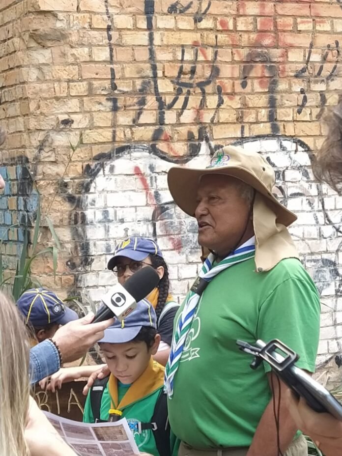 Imagem do WhatsApp de 2025-08-06 à(s) 19.09.19_ac975899 Grupo de escoteiros e moradores reunidos em frente a mural histórico na Candangolândia durante a Trilha Pirá-Brasília.